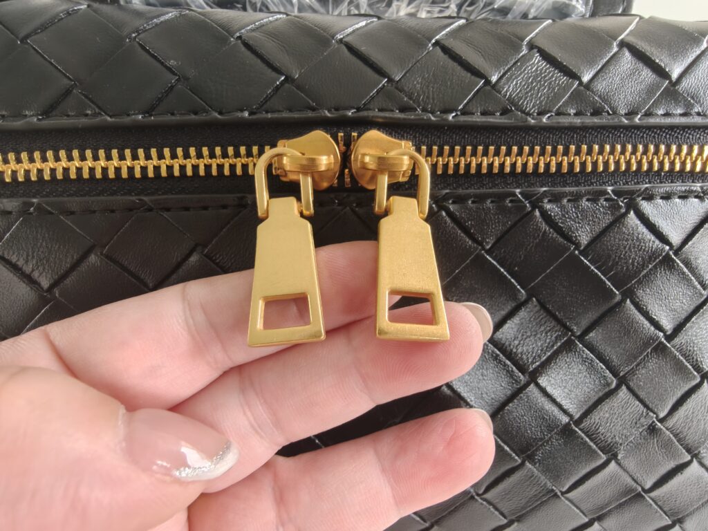 Gold zipper puller and metal zipper quality check on black woven handbag.