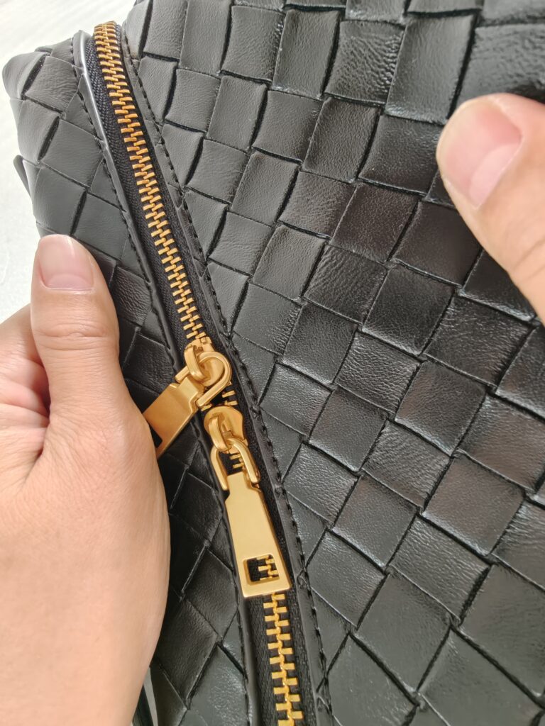 Close up quality inspection of black woven handbag surface stitching and zipper alignment.